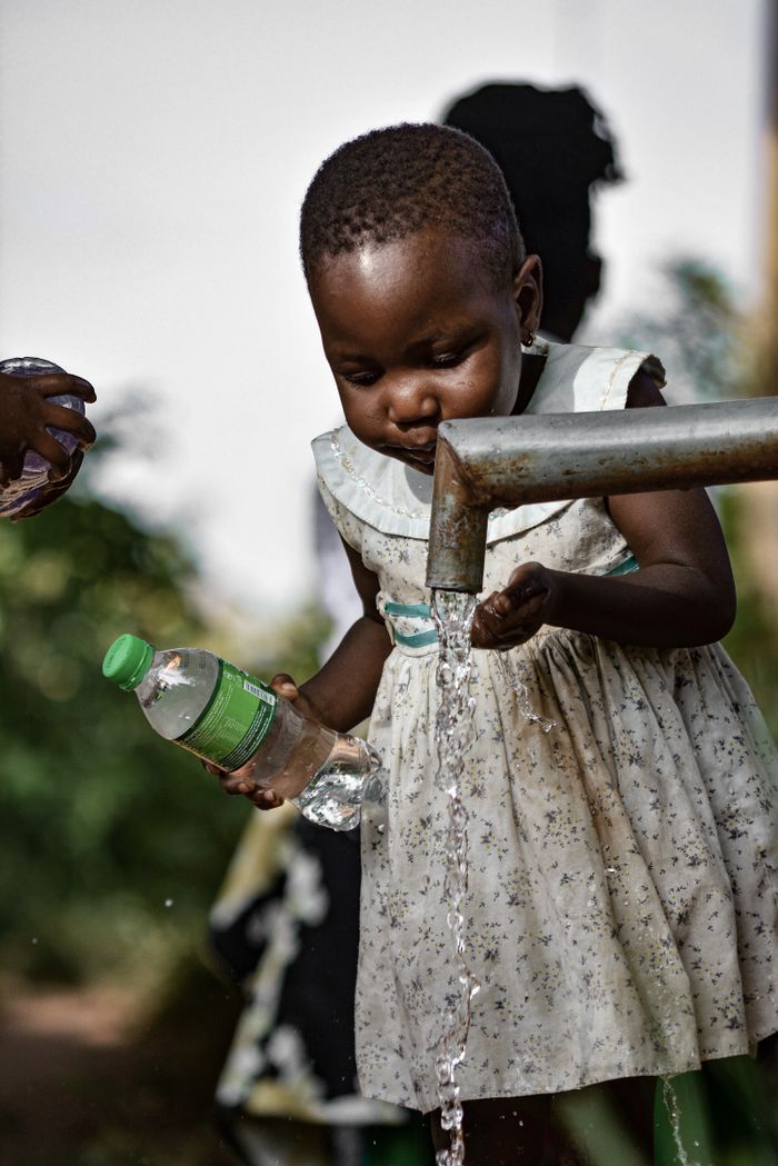 A young girl collects fresh water from a tap in Kampala, Uganda, ensuring water safety.